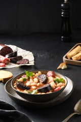 Asturiana stew fabada with chorizo, sausage, haricot on black background. Tasty traditional spanish warming dinner. Vertical format.