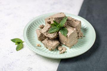 Pieces of halva on green plate. Sweet dessert with mint leaves on white background