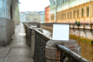 An empty white notebook with space for text stands on the embankment of the Neva River canal in St. Petersburg, mock up