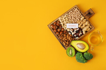 Board with healthy products rich in vitamin E on color background