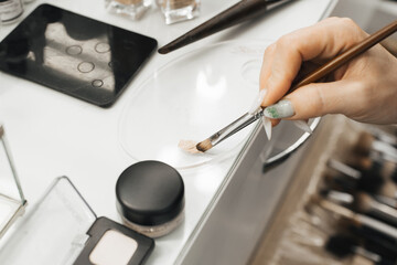 A woman's hand holds makeup brushes and dials a cosmetic product onto the brush. close-up