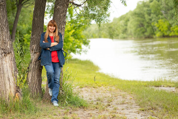 a woman stands on the riverbank near a tree