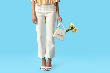 Beautiful young woman with narcissus bouquet and bag on color background