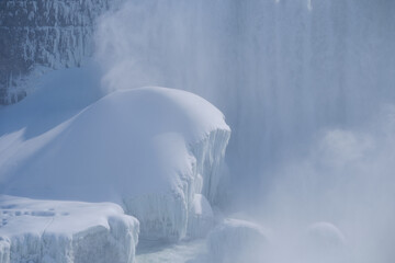 Fine Spray Mist rises off the bottom of the partially frozen over waterfalls in Ontario Canada side of Niagara Falls with ice and snow covering everything