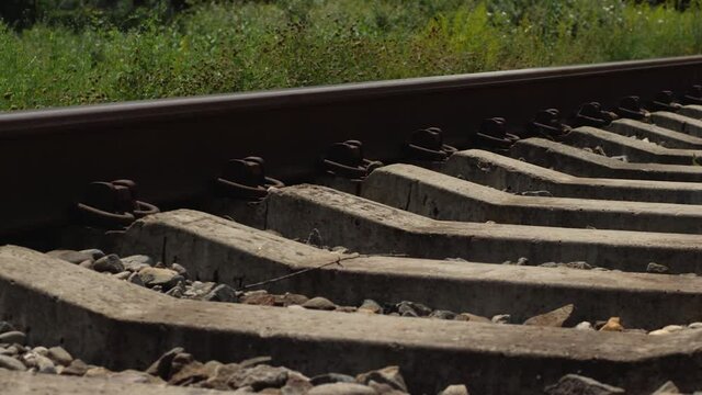 Railway tracks and sleepers are covered with gravel against the background of grass and forest. Camera movement from right to left