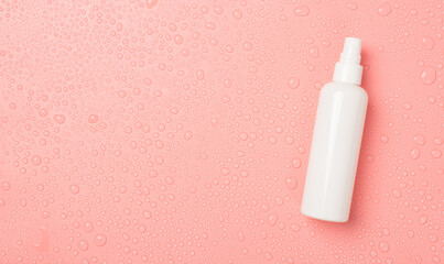 Top view photo of spray bottle without label on the right and water drops on isolated pink...