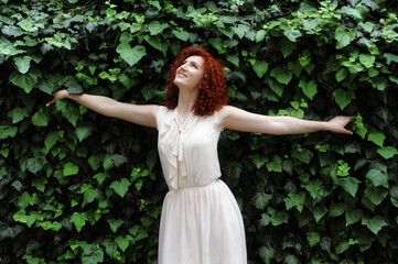 Young beautiful red-haired woman in blossoming flowers garden.