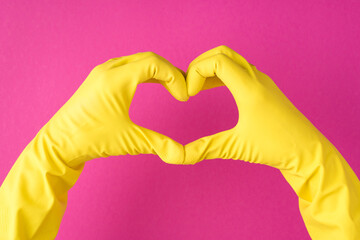 Top view photo of hands in yellow gloves making heart with fingers on isolated pink background with copyspace