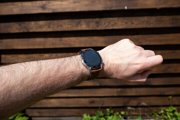Smart watch on a man's hand on the background of a wooden fence.