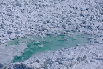Chunks of ice surround a large pool of shallow clear water at the base of the Niagara waterfalls as seen from the Canadian side
