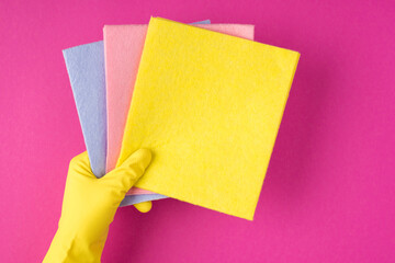 Top view photo of hand in yellow glove holding pink blue and yellow napkins on isolated pink background with copyspace