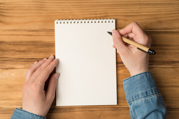 Obraz premium First person top view photo of hands holding pen over copybook on isolated wooden desk background with blank space