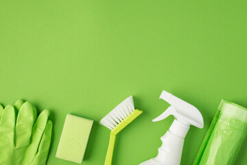 Top view photo of white detergent spray bottle brush sponge garbage bags and green rubber gloves on isolated green background with blank space