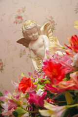 Lovely angel in flowers. Cherub sitting in the flowers of the daylily. Love symbol. Little angel figurine.