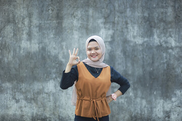 Portrait of young Asian muslim lady wearing hijab shows thumbs up gesture, smiling happy face, approved OK sign
