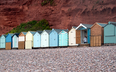 Woman painting the inside of a beach cabin in a row of colorful beach huts