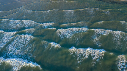 Aerial image of beautiful beach with view of ocean waves and water crashing on to sandy shore from top angle