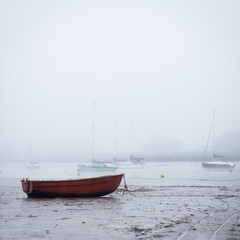 Fototapeta na wymiar Small boats moored on the estuary at low tide as the fog rolls in
