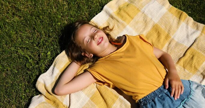 Child lying on the blanket, on the grass in the sun day, little girl take sunbathes on backyard of the house on a sunny summer day, summer time vacation.
