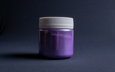 A pot containing resin of a purple glitter color on a dark black background. Used for various purposes in industry and at home in the adaptation of furniture and objects for interior decoration.