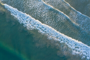 Aerial image of beautiful beach with view of ocean waves and water crashing on to sandy shore from top angle