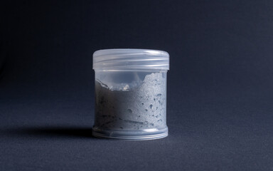A pot containing resin of a white glitter color on a dark black background. Used for various purposes in industry and at home in the adaptation of furniture and objects for interior decoration.