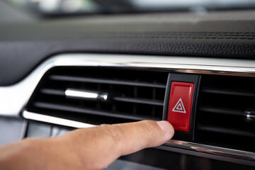 Driver pressing on hazard button on a car dashboard close up with audio and entertainment control panel.