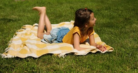 Child lying on the blanket, on the grass in the sun day, little girl take sunbathes on backyard of the house on a sunny summer day, summer time vacation.