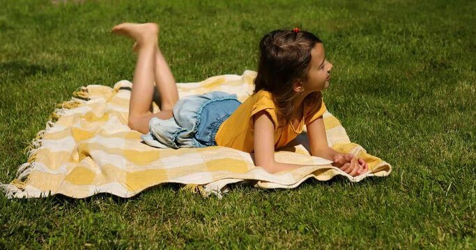 Child lying on the blanket, on the grass in the sun day, little girl take sunbathes on backyard of the house on a sunny summer day, summer time vacation.