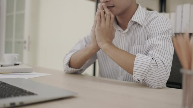 The stressed businessman put their hands in prayer pray and looking laptop with hope pondering reflecting concern about problem challenge sit at the office