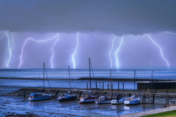Boats in the harbor of Eckwarderhörne / Germany and lightning over the North Sea in the background  - obrazy, fototapety, plakaty