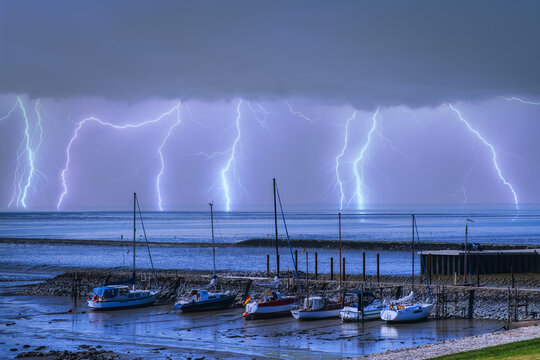 Boats in the harbor of Eckwarderhörne / Germany and lightning over the North Sea in the background 