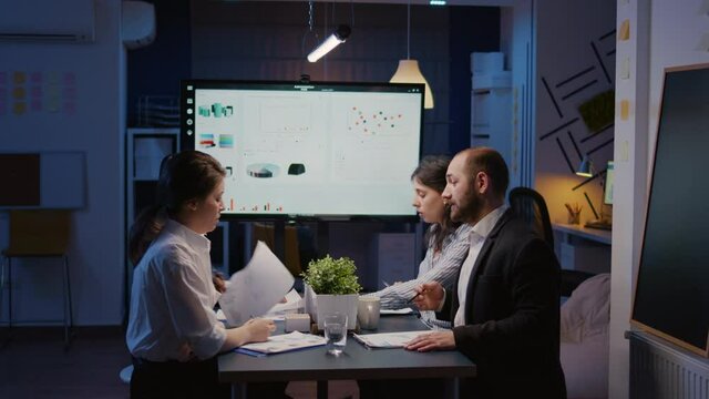 Diverse multi-ethnic group of businesspeople looking at financial presentation on monitor brainstorming company ideas. Teamwork overworking in office meeting room late solving corporate strategy