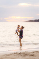 Mother and baby boy playing on beach and sea with sunset.