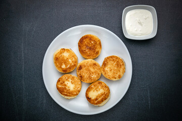 Cheesecakes on a dark table with sour cream
