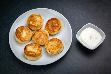 Cheesecakes on a dark table with sour cream
