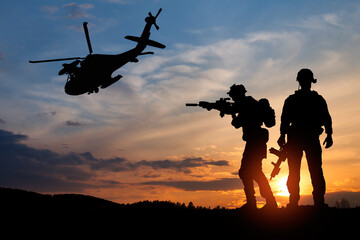 Naklejka na ściany i meble Silhouette of a soldiers and helicopter on the background of sunset. Concept - protection, patriotism, honor.