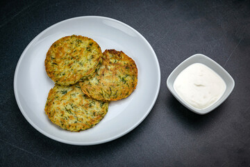 Draniki with sour cream on a dark table
