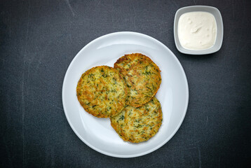 Draniki with sour cream on a dark table
