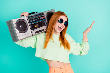 Photo portrait of red haired girl smiling keeping boom box enjoying music isolated vibrant teal...