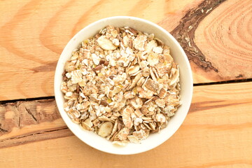 Organic uncooked oat flakes in a white dish on a wooden table, close-up, top view.