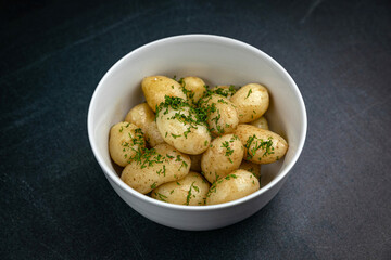 young boiled potatoes with butter, herbs on a dark table
