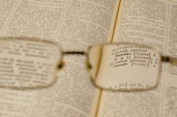 Fototapeta premium Reading glasses and an open book in close-up. Selective Focus on the word RUSSIAN.