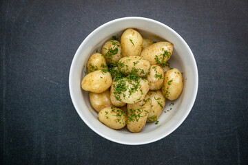 young boiled potatoes with butter, herbs on a dark table
