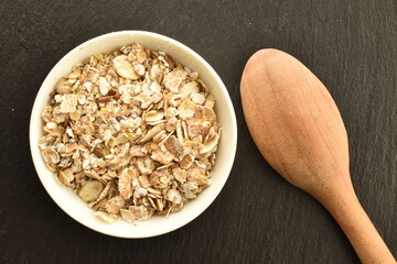 Organic uncooked oat flakes in a white dish on a slate board with a wooden spoon, close-up, top...