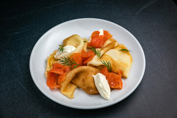 Pancakes with goat cheese and salmon on a dark table

