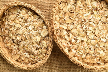 Organic uncooked oat flakes in a straw dish on a jute fabric, close-up, top view.