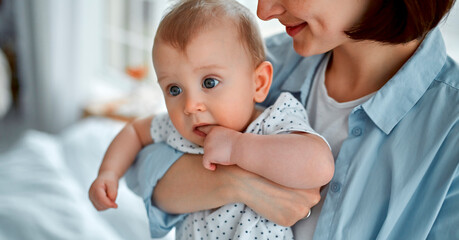 Loving mom carying of her newborn baby at home.Mom and baby boy playing in sunny bedroom. Parent and little kid relaxing at home. Family having fun together. Childcare, maternity concept.