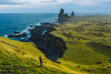 Man hiker in yellow jacket stand on the peak of the rock in outdoor park in Iceland. Londrangar