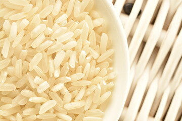 White organic raw rice in a white plate on a vine mat, close-up, top view.